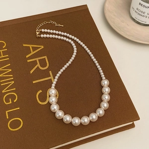 Détail d'un collier de perles dégradées avec fermoir doré sur une surface de livre