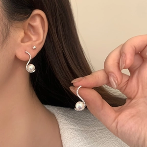 Macro view of S-shaped silver earrings with sparkling zircon and round white mabe pearls