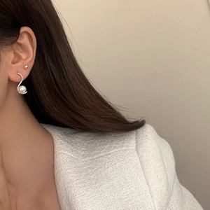 Close-up of elegant S-shaped zircon pearl drop earring and silver stud worn by model