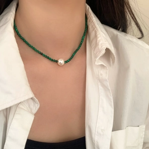 Détail d'un collier en perles de malachite turquoise avec une perle blanche sur un mannequin