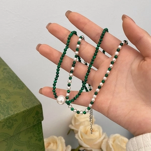 Détail d'un collier de perles en malachite et perles blanches tenu à la main