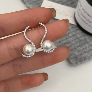 Detailed view of S-shaped wave earrings with pave zircons and white pearls held in hand