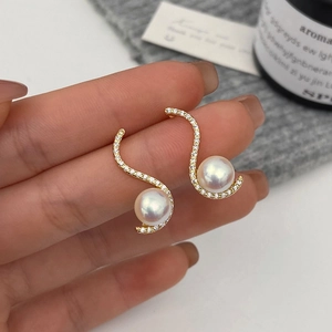Detailed view of S-shaped pearl earrings with gold setting and shimmering zircon accents