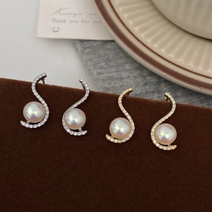 Macro detail of S-shaped pearl earrings with cubic zirconia in gold and silver finish