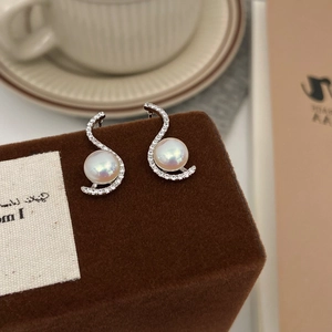 Close-up of S-shaped silver pearl earrings with zircon stones on a brown velvet box