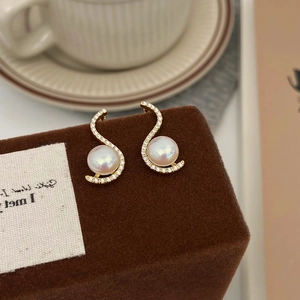 Close-up of elegant S-shaped gold earrings with white pearls and sparkling zircon accents