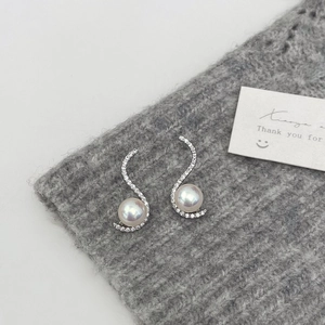 Macro shot of S-shaped silver pearl earrings with micro-pave zircons on knit background