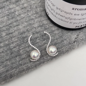 Macro view of S-shaped silver earrings with sparkling zircon and white pearls