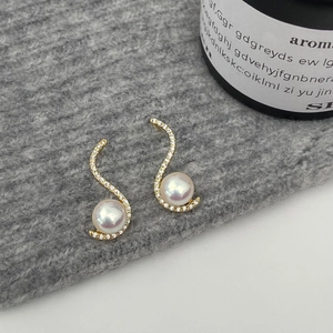 Detail view of gold S-curve earrings with white pearls and sparkling zircons on fabric