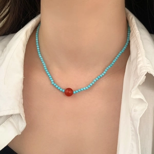 Detail of blue turquoise beaded necklace with orange accent bead on model