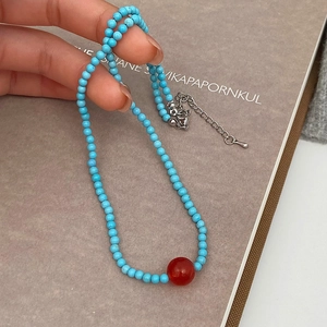 Detailed close-up of turquoise beaded necklace featuring a central red agate bead focal point