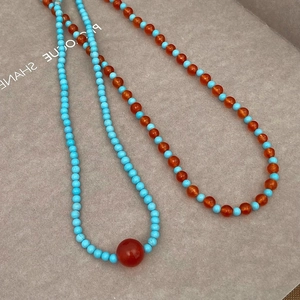 Detail of beaded turquoise and red necklaces with contrasting smooth round stones