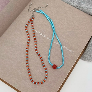Close-up of turquoise and orange beaded necklaces with lobster clasp on vintage book pages