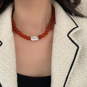 Detail of handmade red agate beaded necklace with a baroque pearl on a white blazer