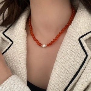 Detail of red agate bead necklace featuring a central white pearl and gold spacers