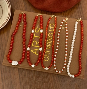 Detailed set of five red agate and pearl necklaces displayed on a vintage brown fabric board