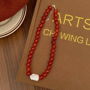 Detail of red agate bead necklace featuring a large baroque pearl and gold clasp