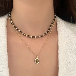 Collier double rang doré avec perles œil de tigre et pendentif ovale sur tissu blanc