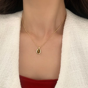 Gros plan du pendentif œil-de-tigre vintage sur chaîne dorée porté sur un haut blanc