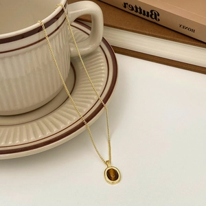 Détail du pendentif œil de tigre vintage sur chaîne dorée près d'une tasse