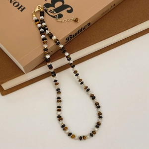Gros plan du collier en perles d'œil de tigre avec fermoir mousqueton doré sur livres anciens