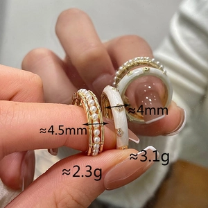 Close-up of a gold pearl eternity band and a white enamel flower ring with weight details