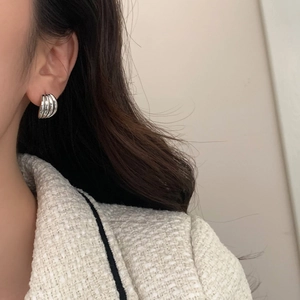 Macro view of silver layered ribbed hoop earring worn by a model in a white tweed jacket