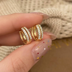 Detail of gold huggie earrings with double row cubic zirconia held between fingers