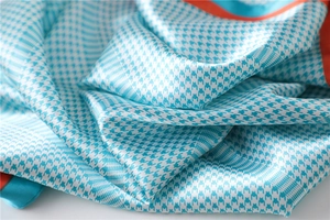 Macro shot of satin houndstooth silk scarf with sky blue pattern and orange borders