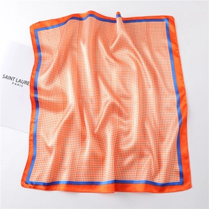 Detailed view of square silk scarf featuring orange houndstooth pattern and blue borders