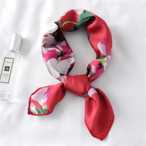 Detail showing red floral silk scarf tied in a neat knot on white fabric texture