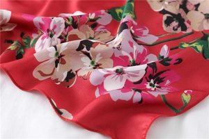 Detail shot of a red floral silk scarf showing premium texture and neat hemmed edges