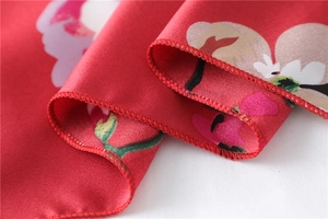 Macro shot of red floral silk scarf showing fine overlock stitching and satin texture
