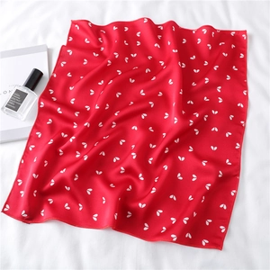 Detail of red satin square scarf with white heart prints on a white fabric surface