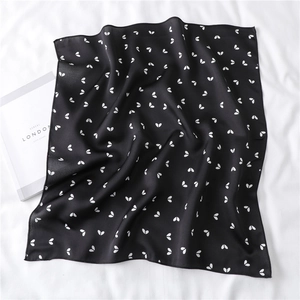 Detailed close-up of a black silk scarf with small white heart prints on white fabric