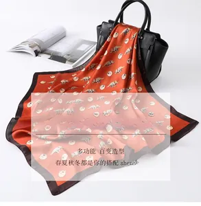 Close-up of orange silk scarf with dinosaur patterns styled on a black leather handbag