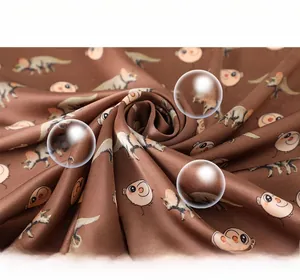 Close-up of brown silk-like fabric showing detailed cartoon dinosaur patterns and texture