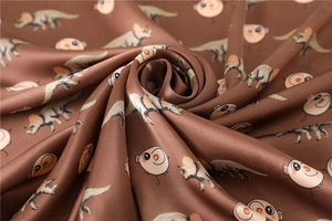Detail of satin silk scarf featuring cartoon dinosaur prints on a brown fabric background