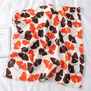 Detail showing orange ginkgo leaf pattern and fine hemmed edges on a cream square scarf