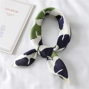 Detailed close-up of a white silk scarf with blue and green tropical leaf patterns