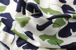 Detailed macro view of smooth satin scarf fabric featuring blue and green ginkgo leaves