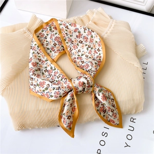 Détail d'un foulard en soie à fleurs avec bordure orange sur une chemise plissée