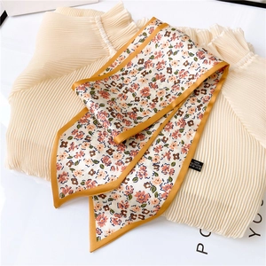Détail d'un foulard étroit à fleurs avec bordure jaune sur un chemisier plissé beige