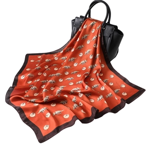70cm orange silk scarf with cartoon dinosaur prints draped over a black leather handbag