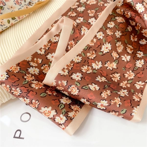 Détail d'un foulard étroit en soie marron vintage avec motifs marguerites et satin