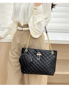 Detail of black quilted barrel bag featuring gold chain and flamingo charm accessory