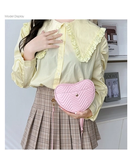 Detail of pink heart-shaped crossbody bag featuring quilted texture and golden hardware