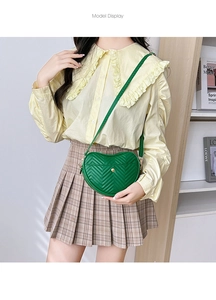 Green heart-shaped leather crossbody bag with V-quilted stitching shown on a model