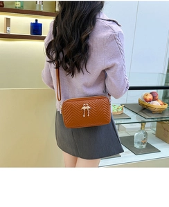 Brown quilted crossbody bag with V-shaped texture and gold metal charm accessory