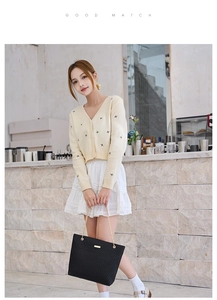 Close-up of black quilted chain shoulder bag paired with yellow knit cardigan and white skirt